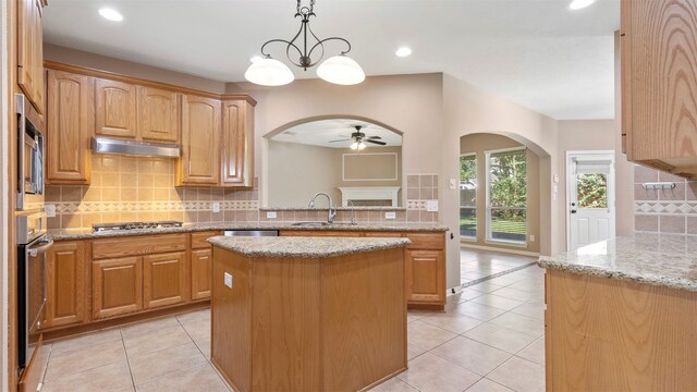 kitchen featuring ceiling fan with notable chandelier, pendant lighting, a kitchen island, and light stone countertops