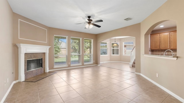 unfurnished living room featuring a fireplace, light tile patterned flooring, sink, and ceiling fan