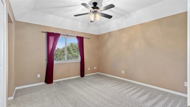 empty room featuring a raised ceiling, light colored carpet, and ceiling fan