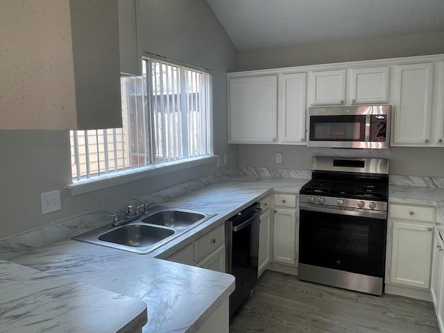 kitchen with stainless steel appliances, sink, vaulted ceiling, and white cabinetry