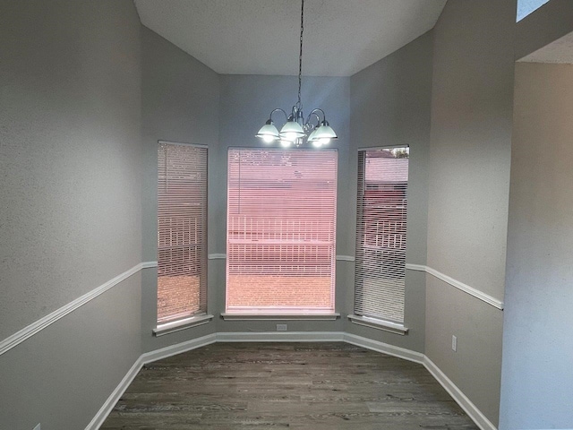 unfurnished dining area with dark hardwood / wood-style flooring, a notable chandelier, and lofted ceiling