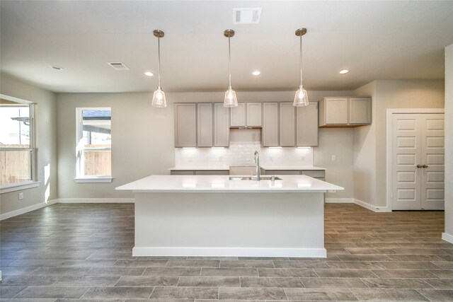 kitchen featuring gray cabinetry, sink, an island with sink, and dark wood-type flooring