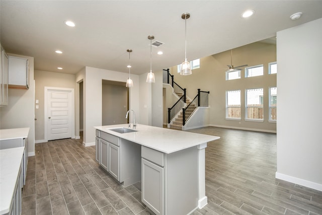 kitchen with ceiling fan, sink, decorative light fixtures, light hardwood / wood-style floors, and an island with sink