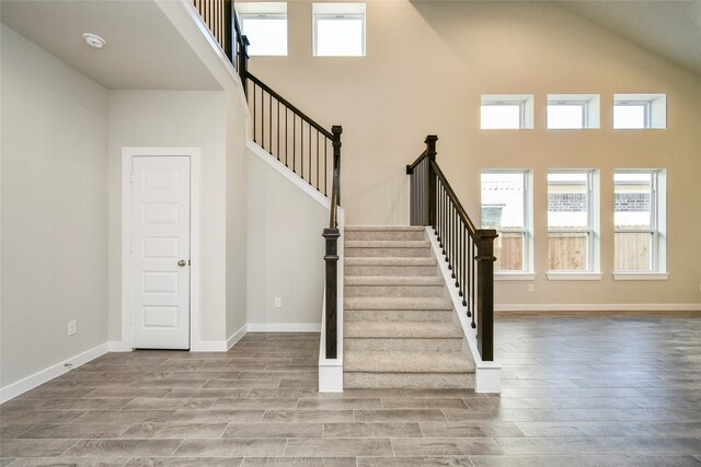 stairway with hardwood / wood-style floors and high vaulted ceiling