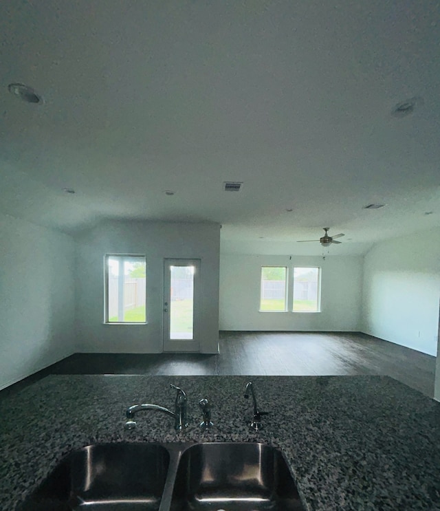 kitchen with dark stone counters, sink, ceiling fan, and dark wood-type flooring