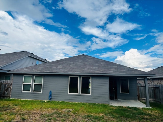 rear view of property featuring a yard, roof with shingles, a patio, and fence