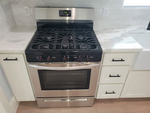 kitchen with white cabinetry, stainless steel gas range oven, and decorative backsplash