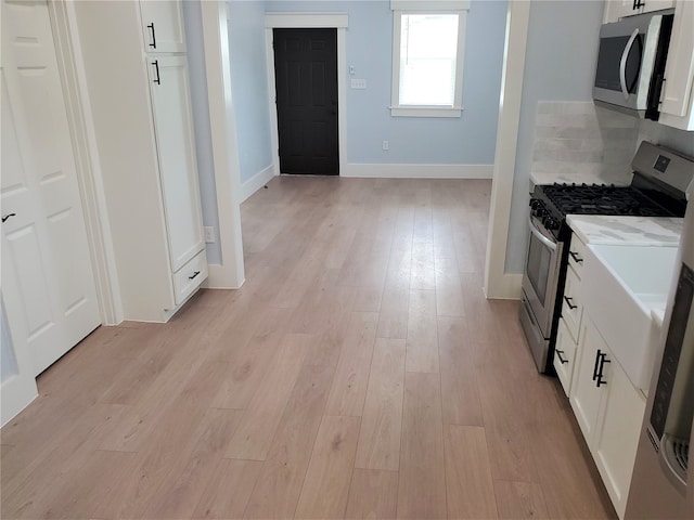 kitchen featuring light wood-type flooring, light stone countertops, stainless steel appliances, and white cabinets