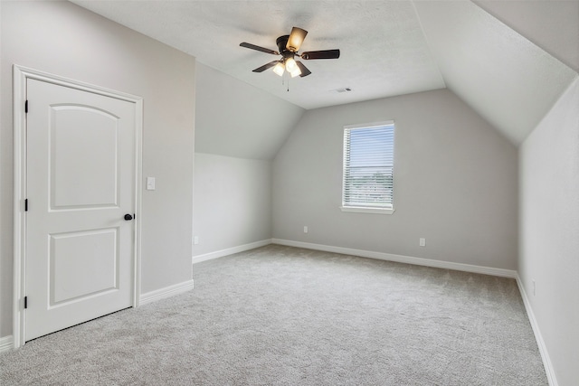 additional living space featuring a textured ceiling, vaulted ceiling, light carpet, and ceiling fan