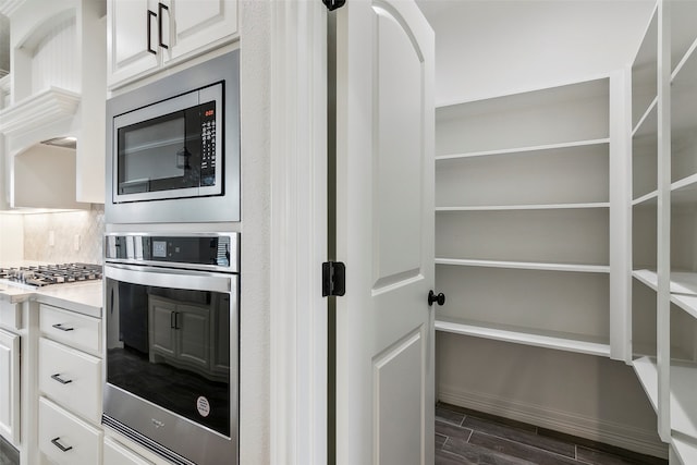 kitchen with dark wood-type flooring, appliances with stainless steel finishes, white cabinetry, and tasteful backsplash