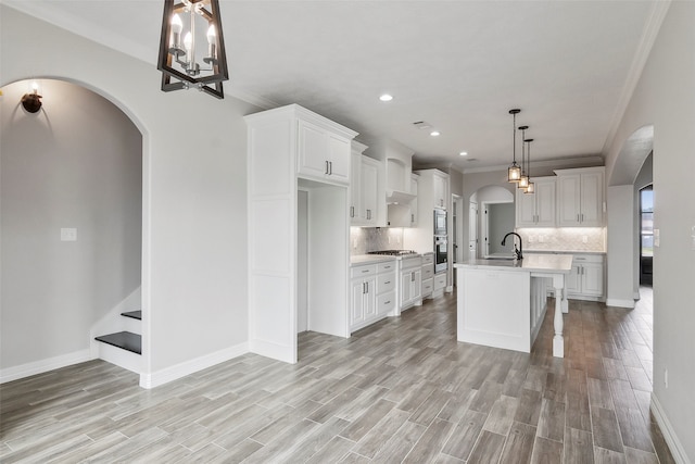 kitchen featuring pendant lighting, tasteful backsplash, an island with sink, a breakfast bar, and white cabinetry