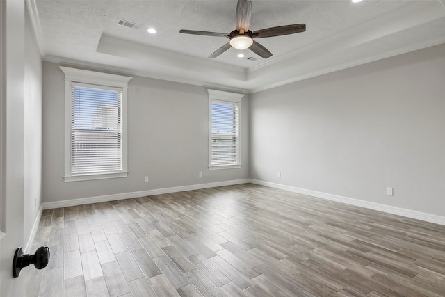 empty room with ornamental molding, a textured ceiling, light hardwood / wood-style flooring, ceiling fan, and a raised ceiling