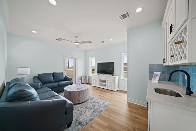 living room with crown molding, ceiling fan, sink, and light wood-type flooring