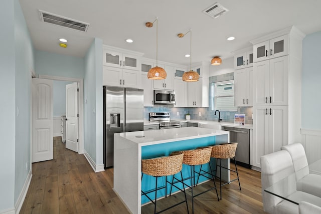 kitchen featuring a kitchen bar, white cabinetry, hanging light fixtures, a kitchen island, and stainless steel appliances