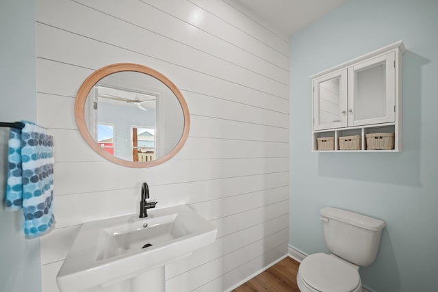 bathroom with hardwood / wood-style flooring, sink, wooden walls, and toilet