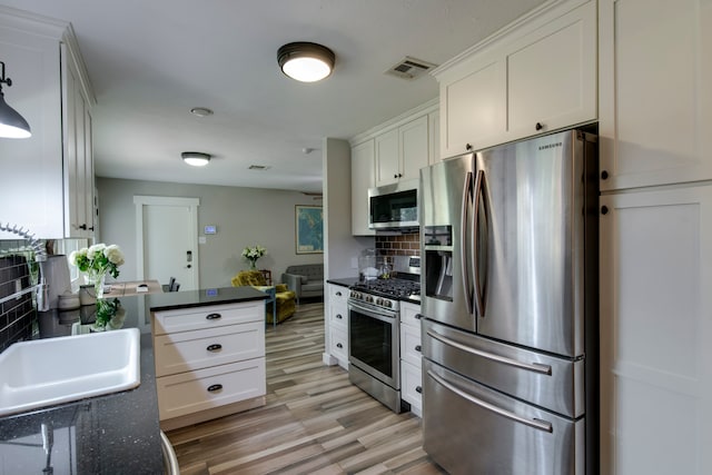 kitchen with appliances with stainless steel finishes, light hardwood / wood-style floors, tasteful backsplash, sink, and white cabinetry