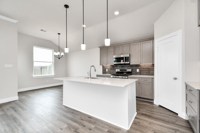 kitchen with vaulted ceiling, gray cabinetry, pendant lighting, appliances with stainless steel finishes, and a kitchen island with sink