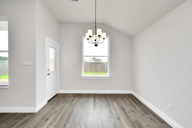 unfurnished dining area featuring vaulted ceiling, an inviting chandelier, and hardwood / wood-style flooring