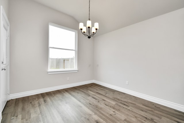 spare room with wood-type flooring, a notable chandelier, and vaulted ceiling