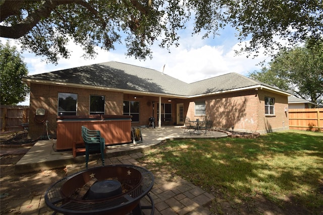 rear view of house featuring a lawn, a patio area, a hot tub, and a fire pit