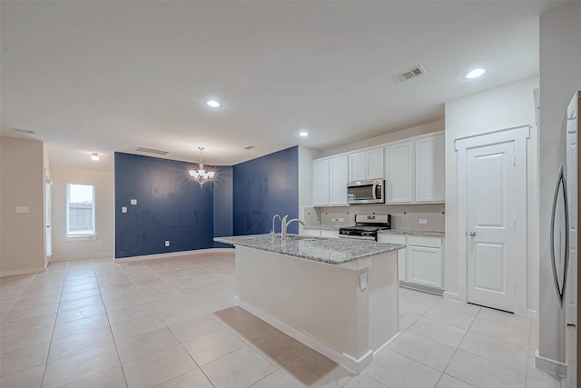 kitchen with sink, an island with sink, appliances with stainless steel finishes, light stone counters, and white cabinetry