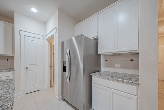 kitchen with white cabinets, decorative backsplash, stainless steel fridge, and light stone counters