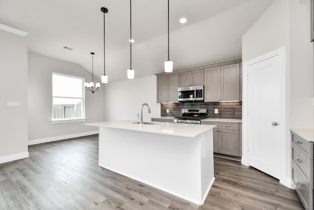 kitchen featuring stainless steel appliances, lofted ceiling, gray cabinets, an island with sink, and pendant lighting