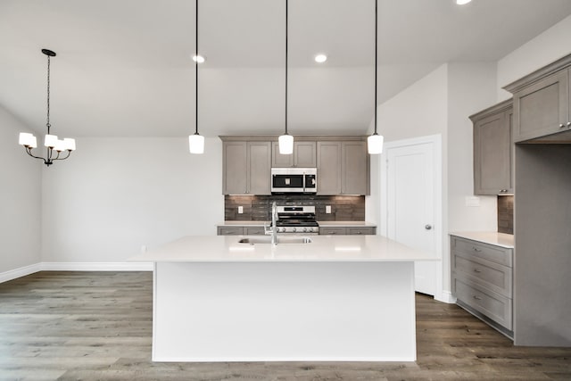 kitchen with appliances with stainless steel finishes, tasteful backsplash, a center island with sink, and hanging light fixtures