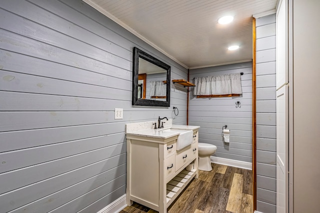 bathroom with wood-type flooring, toilet, wooden walls, and vanity