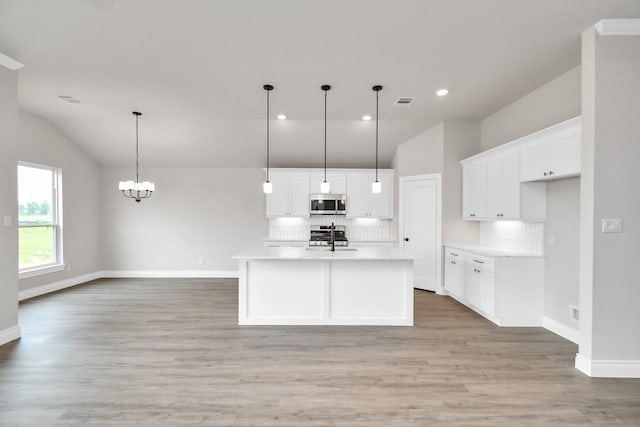 kitchen with lofted ceiling, stainless steel microwave, white cabinets, and decorative backsplash