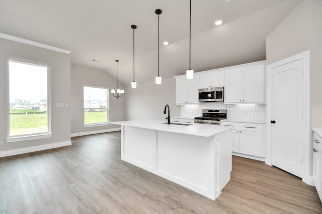 kitchen with pendant lighting, appliances with stainless steel finishes, sink, lofted ceiling, and white cabinets