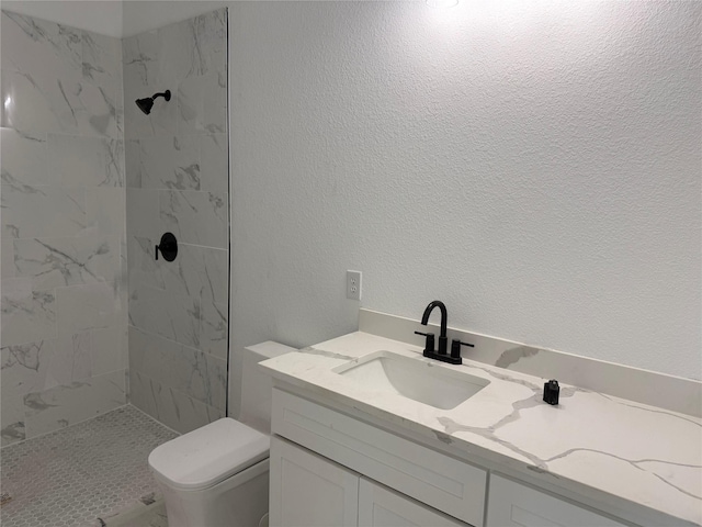 bathroom with tiled shower, vanity, and toilet