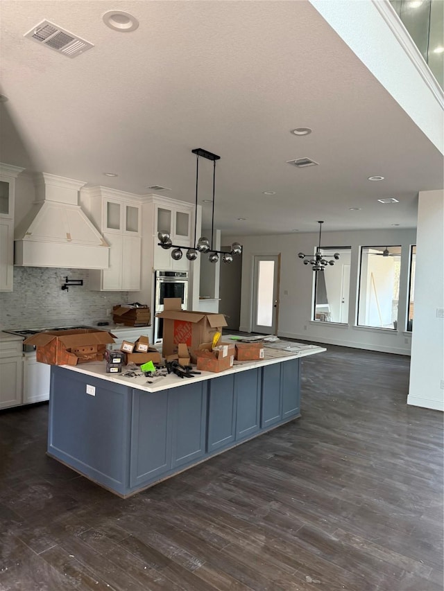 kitchen featuring a large island, white cabinets, decorative light fixtures, and custom range hood