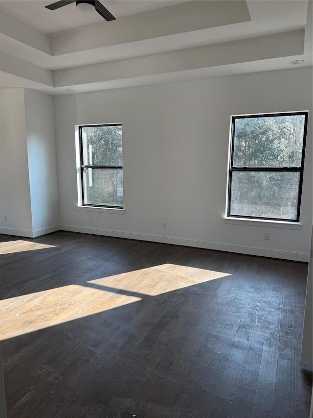 empty room featuring ceiling fan, a raised ceiling, and dark wood-type flooring