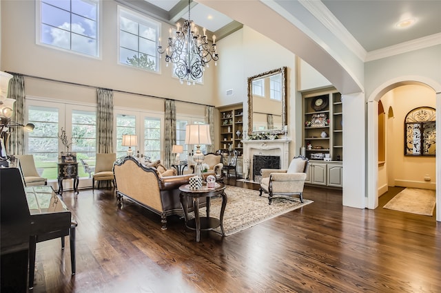 living room with dark wood-type flooring, built in features, a notable chandelier, and ornamental molding