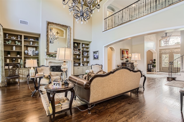 living room with a high ceiling, built in features, dark hardwood / wood-style floors, and an inviting chandelier