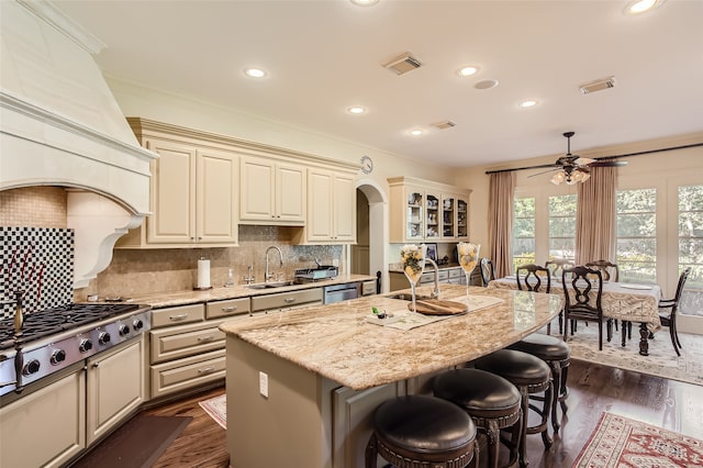 kitchen featuring light stone counters, an island with sink, cream cabinetry, ceiling fan, and a breakfast bar