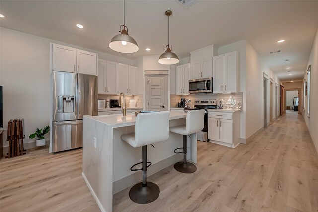 kitchen featuring light wood-type flooring, appliances with stainless steel finishes, a center island with sink, and white cabinetry