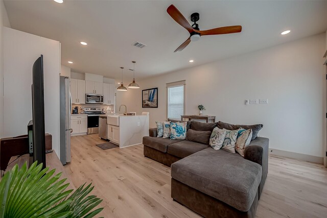 living room featuring light hardwood / wood-style flooring, ceiling fan, and sink