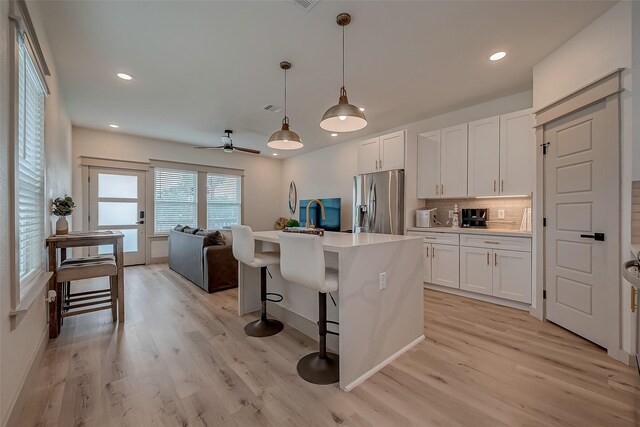 kitchen with stainless steel fridge, light hardwood / wood-style flooring, a kitchen breakfast bar, ceiling fan, and white cabinets