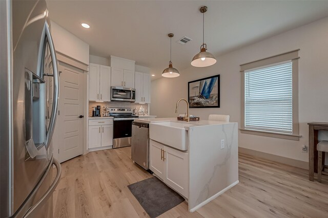 kitchen featuring stainless steel appliances, light hardwood / wood-style floors, white cabinetry, pendant lighting, and a center island with sink