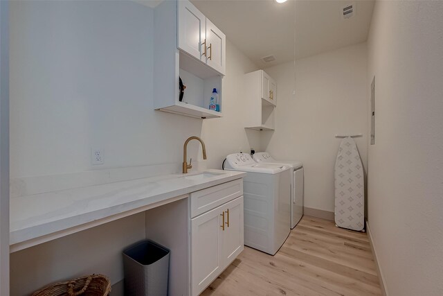 clothes washing area featuring washer and dryer, cabinets, sink, and light hardwood / wood-style flooring