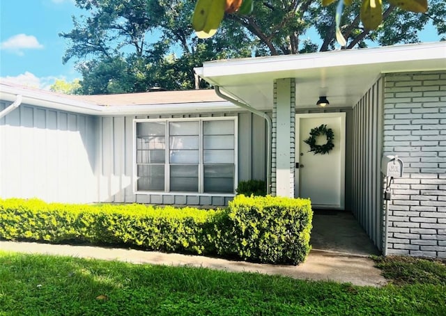 doorway to property featuring board and batten siding and brick siding