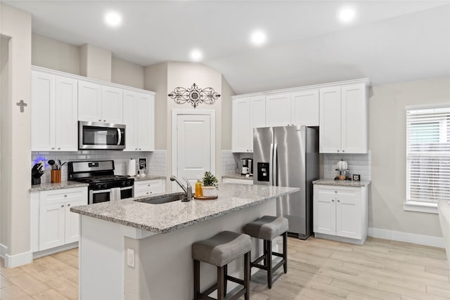 kitchen featuring white cabinetry, appliances with stainless steel finishes, backsplash, vaulted ceiling, and a kitchen island with sink