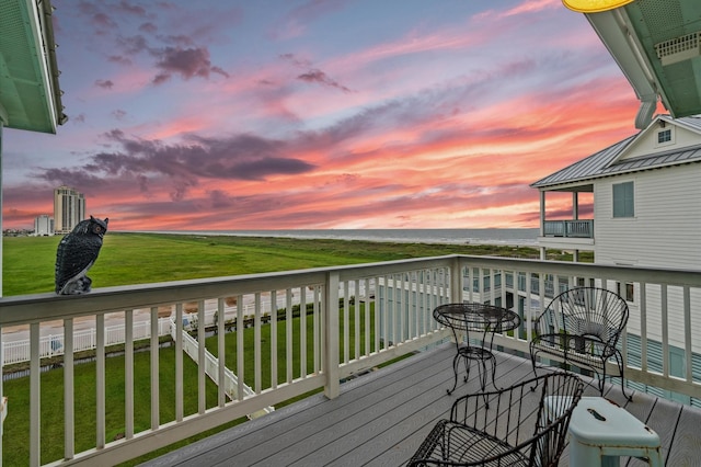 deck at dusk with a water view and a yard