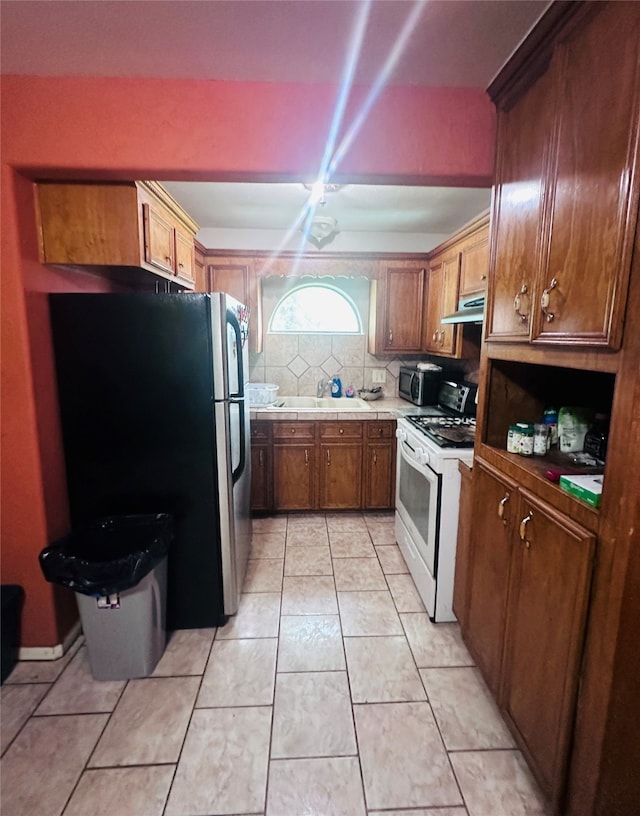 kitchen with stainless steel refrigerator, sink, white gas range oven, light tile patterned flooring, and decorative backsplash