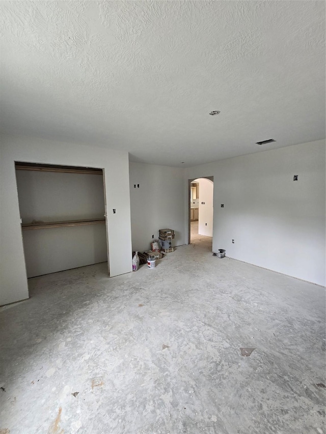 unfurnished bedroom featuring arched walkways, a textured ceiling, and concrete floors