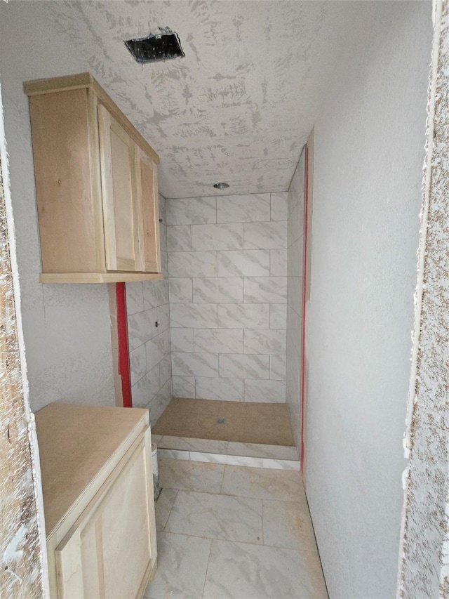 full bathroom featuring a tile shower and marble finish floor