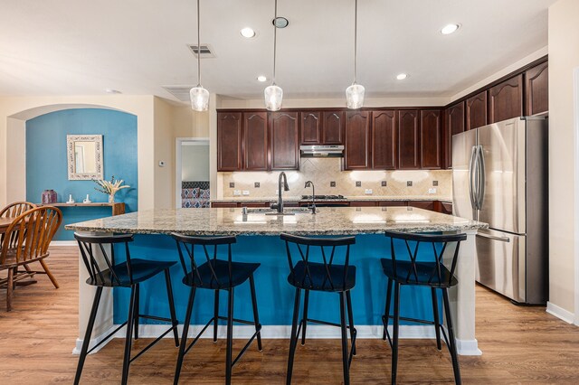 kitchen with light wood-type flooring, stainless steel fridge, backsplash, and an island with sink