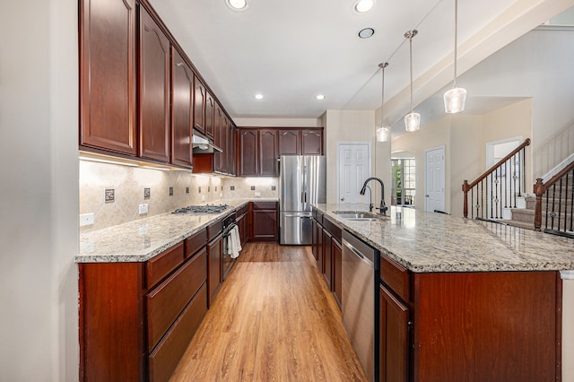 kitchen featuring stainless steel appliances, decorative light fixtures, sink, a center island with sink, and light hardwood / wood-style floors